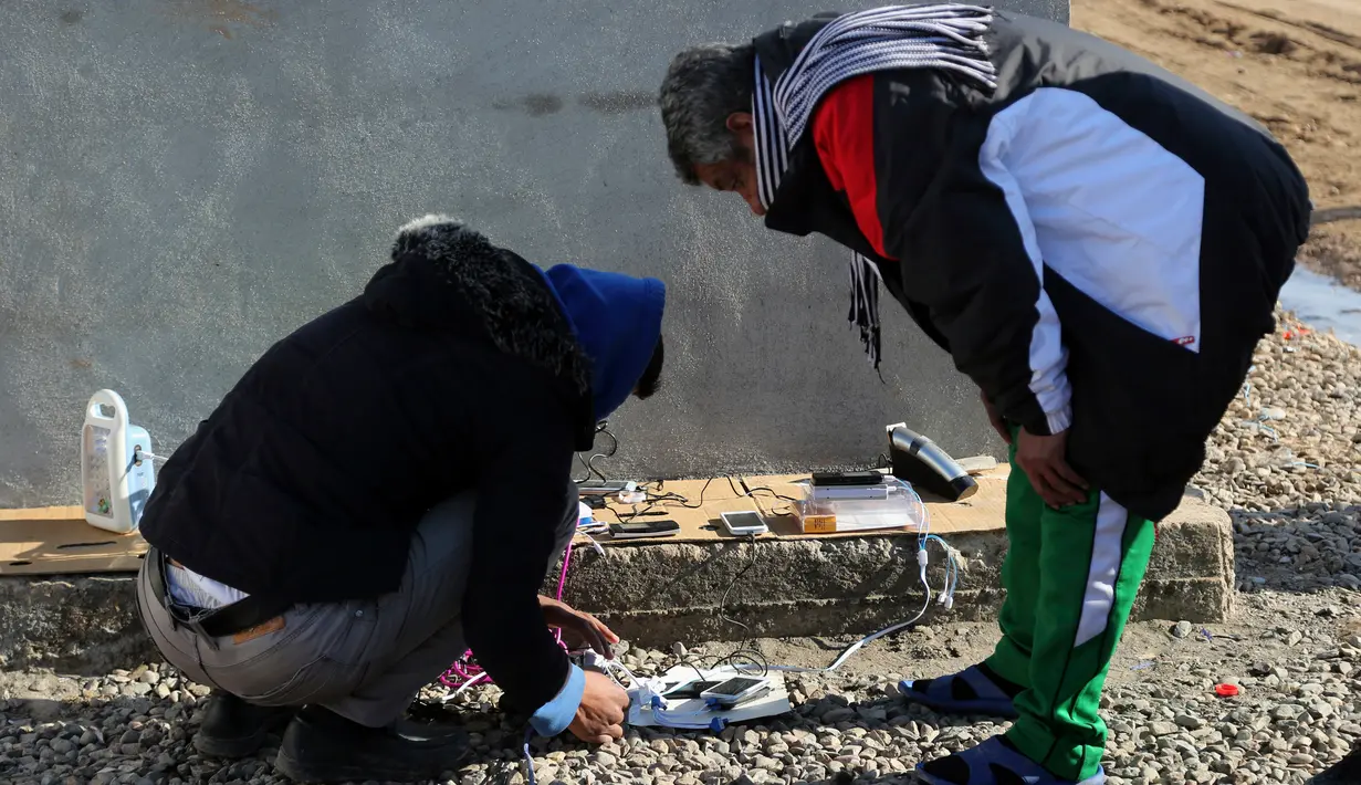 Sejumlah Warga mengisi daya ponsel dan lentera mereka dengan membayar biaya untuk generator sebesar Rp 5.700 di kamp pengungsian Sewdinan, Khazer, Irak, 3 Januari 2017. (AP Photo/Khalid Mohammed)