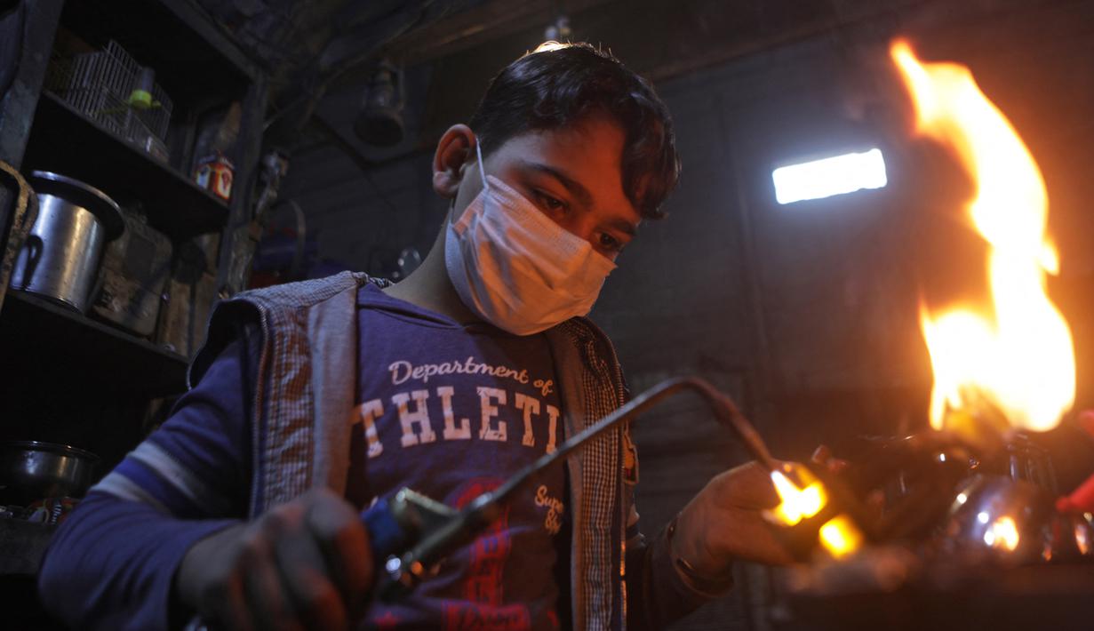 Nadim al-Nako (12) bekerja membuat panci dan wajan di bengkel ayahnya di utara Kota al-Bab yang dikuasai Turki, Suriah, 20 November 2021. Menurut UNICEF, setelah satu dekade perang diperkirakan 2,5 juta anak-anak Suriah putus sekolah. (Bakr ALKASEM/AFP)