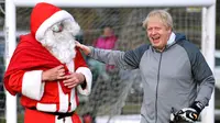PM Inggris Boris Johnson menyapa pria berpakaian Sinterklas sebelum pertandingan sepak bola putri junior antara Hazel Grove United JFC dan Poynton di Cheadle Hulme, Inggris, Sabtu (7/12/2019). Aksi itu dalam rangka kampanye jelang pemilu Inggris 12 Desember 2019. (Toby Melville/Pool Photo via AP)