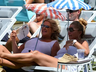 Dua penonton wanita duduk sambil membawa payung kecil menyaksikan serunya pertandingan tenis selama putaran pertama Australian Open 2017 di Melbourne, Australia (16/1). (AFP Photo/Greg Wood)
