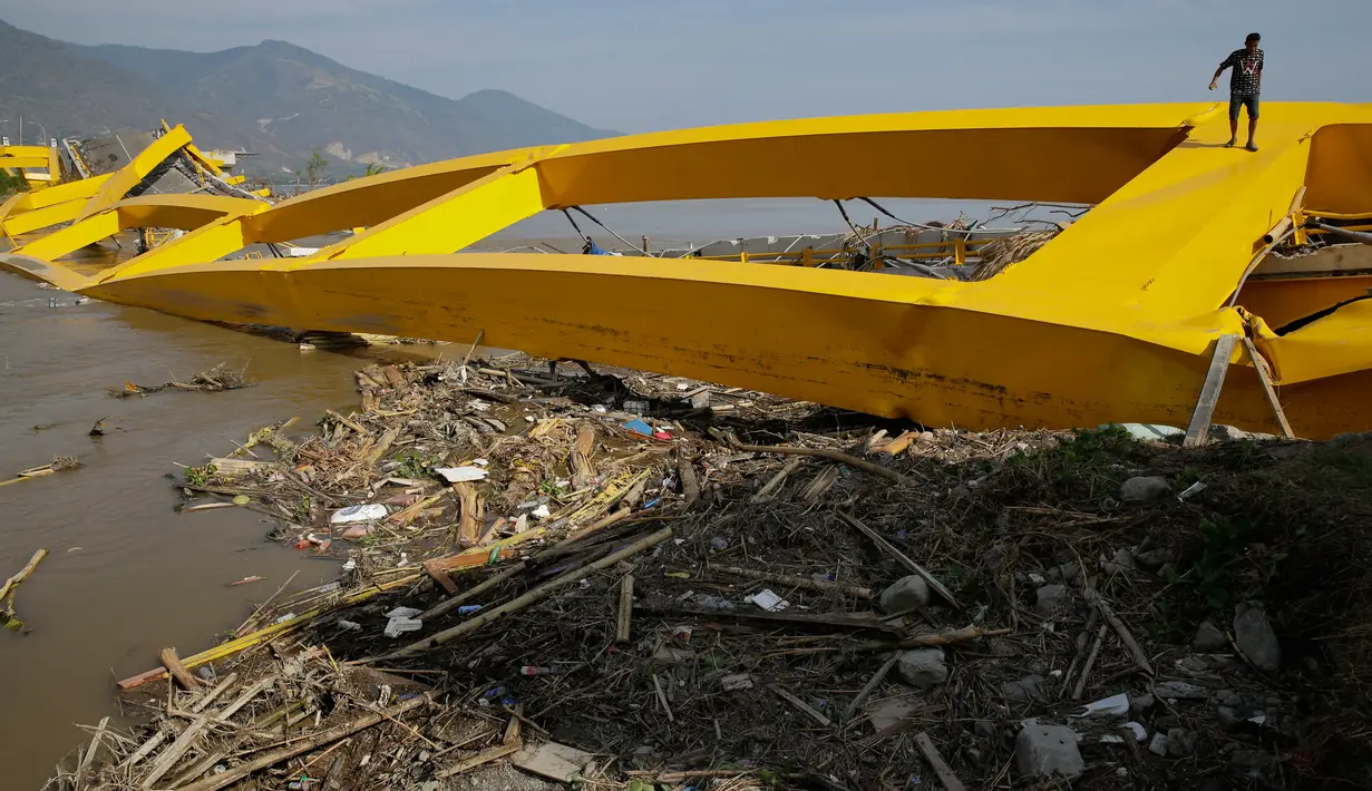 Seorang pria memanjat jembatan yang ambruk akibat gempa dan tsunami di Palu, Rabu (3/10). Jembatan bernama asli Jembatan Palu IV dan biasa disebut Jembatan Ponulele ini diresmikan Presiden Susilo Bambang Yudhoyono pada Mei 2006. (AP Photo/Aaron Favila)