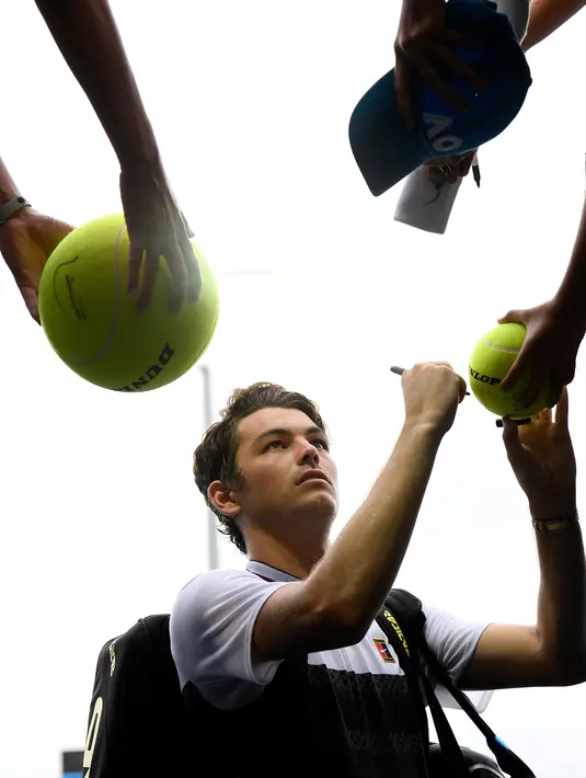 Petenis Amerika Serikat, Taylor Fritz menandatangi bola yang disodorkan penggemarnya setelah mengalahkan Gael Monfils dari Prancis dalam babak kedua  turnamen Australia Terbuka di Melbourne, Rabu (16/1). (AP Photo/Andy Brownbill)
