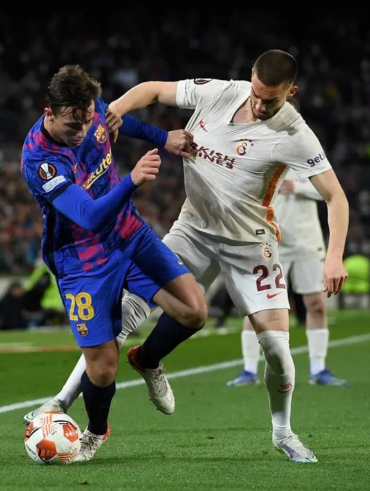 Gelandang Barcelona, Nico Gonzalez (kiri) berebut bola dengan gelandang Galatasaray, Berkan Kutlu selama pertandingan leg pertama babak 16 besar Liga Europa di stadion Camp Nou di Barcelona (11/3/2022). Barcelona bermain imbang atas Galatasaray 0-0. (AFP/Lluis Gene)