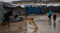 Kurangnya saluran drainase yang memadai dan kerusakan infrastruktur akibat perang yang berlangsung sejak Oktober 2023, membuat air sulit surut. Tampak dalam foto, seorang pria membersihkan air dari tendanya di sebuah kamp pengungsi Palestina setelah hujan deras di Deir al-Balah, Jalur Gaza, Kamis 11 Desember 2025. (AP Photo/Abdel Kareem Hana)