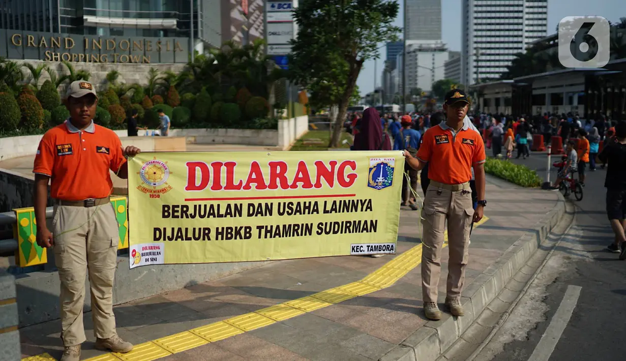 Petugas Satpol PP membentangkan spanduk larangan berjualan di jalur Hari Bebas Kendaraan Bermotor atau Car Free Day, Jakarta, Minggu (3/11/2019). Pemprov DKI melarang PKL berjualan di sepanjang jalur Car Free Day yang selama ini memenuhi badan jalan maupun trotoar. (Liputan6.com/Immanuel Antonius)