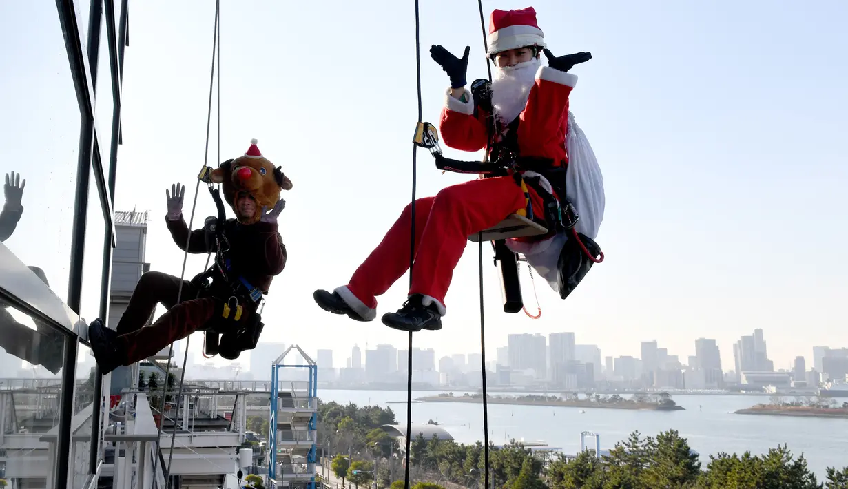 Petugas berkostum Santa Claus dan rusa melambaikan tangan saat membersihkan kaca-kaca gedung bertingkat di pusat perbelanjaan di Tokyo, Kamis (21/12). Wajah sang Santa hampir tak terlihat karena tertutupi jenggot putih dan topinya (AFP/Toshifumi KITAMURA)