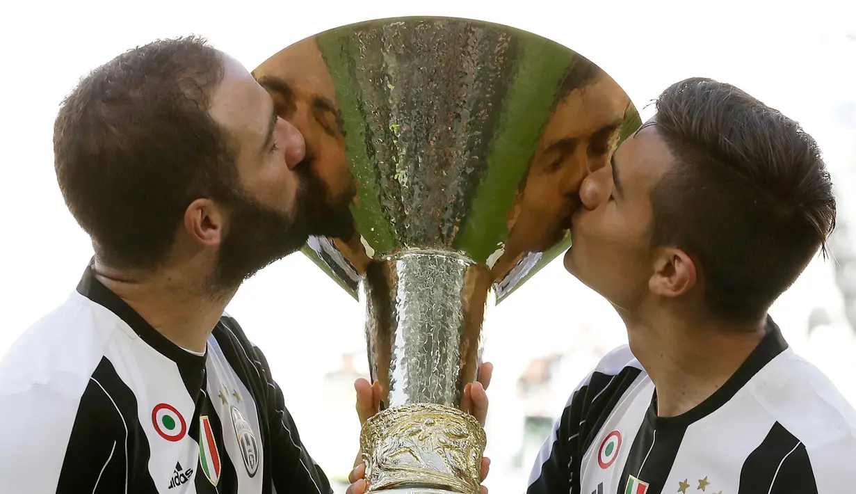Penyerang Juventus, Gonzalo Higuain dan Paulo Dybala mencium trofi Liga Italia di Juventus Stadium, Turin, (21/5). Juventus menjadi tim pertama dalam sejarah yang bisa meraih enam scudetto secara beruntun. (AP Photo/Antonio Calanni)