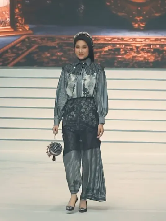 Azizah Salsha mengenakan koleksi Zaskia Sungkar, tampil dengan kemeja lengan panjang hitam bercorak dipadukan celana panjang di atas apron lace hitam. Ia juga mengenakan collar lace hitam senada dengan kerudungnya. [@azizahsalsha_]