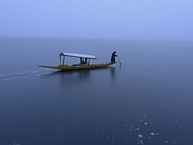 Seorang pria mengendarai perahu di dekat bagian beku danau Dal setelah hujan salju lebat di Srinagar (16/1/2020). Banyak daerah terpencil di lembah telah terputus akibat hujan salju lebat tersebut. (AFP Photo/Tauseef Mustafa)