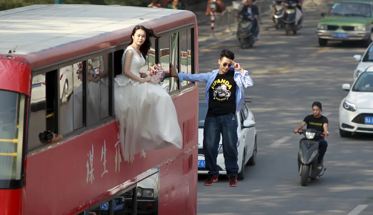 Pesulap Lei Xin (kanan) berada di luar bus tingkat sambil melayang dengan seorang wanita bergaun pengantin di Zhengzhou, Provinsi Henan, China, (15/10/2015). Aksi bertujuan mengajak masyarakat untuk tidak takut menikah diusia muda. (REUTERS/Stringer)