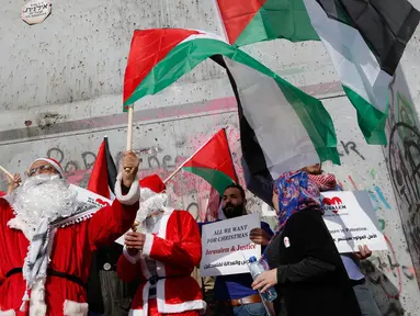 Pengunjuk rasa berkostum sinterklas (Santa Claus) memegang bendera Palestina dalam demonstrasi di Bethlehem, Tepi Barat, 23 Desember 2017. Mereka menentang kebijakan Presiden Donald Trump soal Yerusalem yang diklaim Ibu Kota Israel. (AP/Nasser Shiyoukhi)