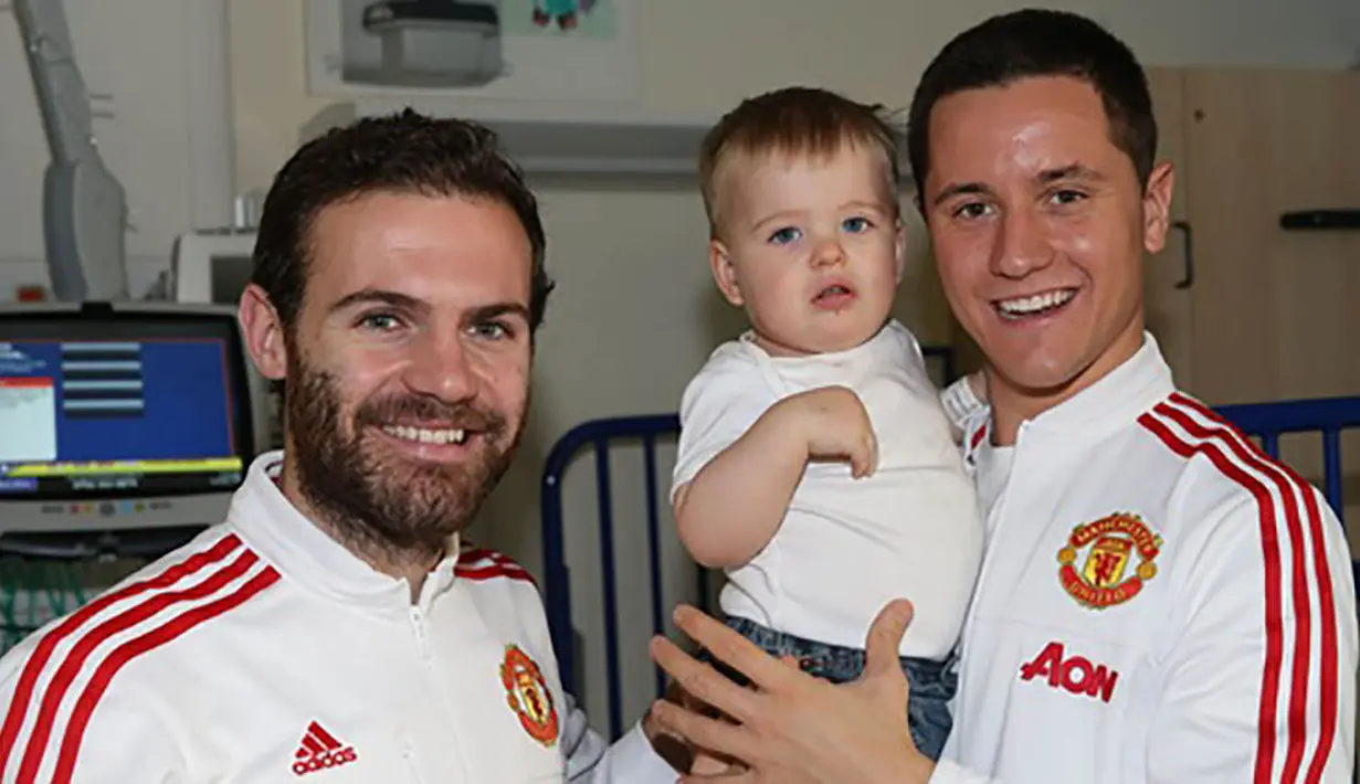 Pemain Manchester United, Ander Herrera, menggendong seorang anak yang sedang sakit saat mengunjungi Rumah Sakit Royal Manchester Children bersama rekan setimnya, Juan Mata. (www.manutd.com)