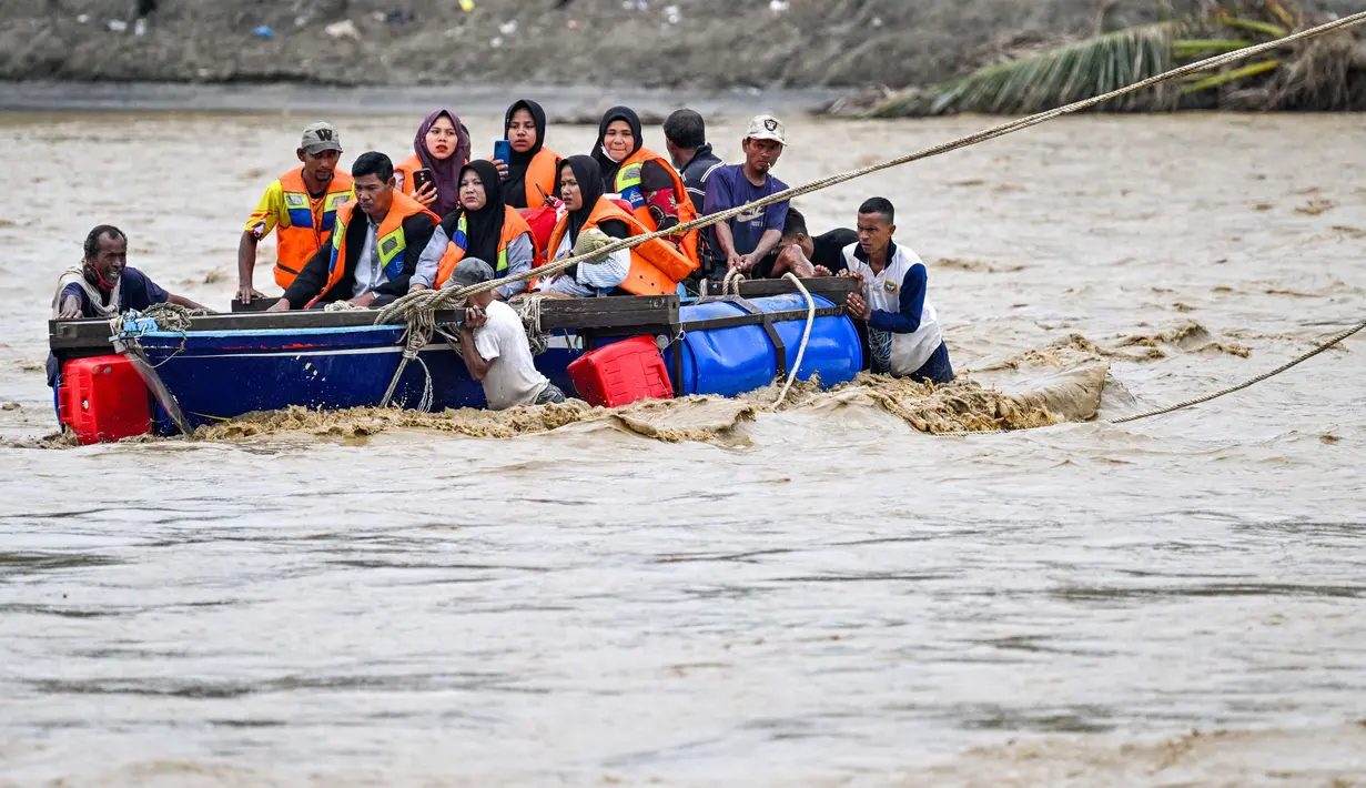 Sebagai informasi, untuk memulihkan akses transportasi, Kementerian PUPR bersama TNI telah membangun jembatan darurat (jembatan bailey) di lokasi tersebut, yang diperkirakan rampung dan mulai bisa dilintasi pada pertengahan Desember 2025. Tampak dalam foto, warga menyeberangi sungai setelah jembatan rusak akibat banjir di Juli, provinsi Aceh, pada Minggu 14 Desember 2025. (CHAIDEER MAHYUDDIN/AFP)