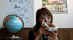 Seorang pengunjung menikmati Mrs. Burger di J.S. Burgers Cafe, Tokyo, Jepang, (7/10). Memeriahkan pilpres AS, kafe di Tokyo ini membuat menu  baru yang unik yakni Mr. dan Mrs. Burger. (REUTERS/Megumi Lim)