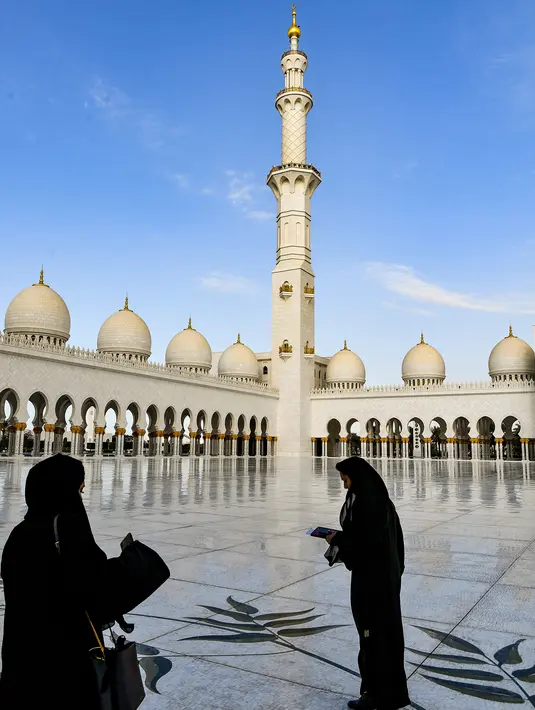 Dua wanita berdiri di halaman Masjid Agung Sheikh Zayed di Abu Dhabi, Uni Emirat Arab. Dibangun dengan 82 kubah bergaya Maroko dan semuanya dihias dengan batu pualam putih. (Photo by Vincenzo PINTO / AFP)