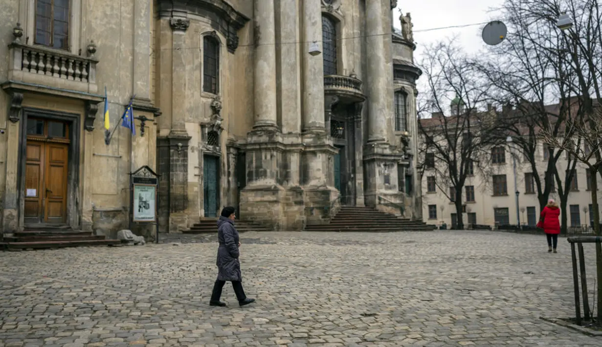 Seorang wanita berjalan melewati Museum Sejarah Agama di Lviv, Ukraina, 4 Maret 2022. Pekerja merakit wadah logam di teras museum untuk menyimpan barang-barang dengan aman sebelum menempatkannya pada ruang bawah tanah untuk berjaga-jaga jika invasi Rusia maju ke barat. (AP Photo/Bernat Armangue)