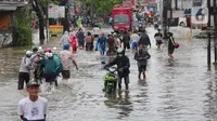 Warga berusaha melintasi genangan air ketika banjir merendam Jalan KH. Hasyim Ashari, Tangerang, Banten, Sabtu (16/7/2022). Akibat luapan kali angke ruas jalan yang menghubungkan Tangerang-Jakarta itu terputus akibat banjir. (Liputan6.com/Angga Yuniar)