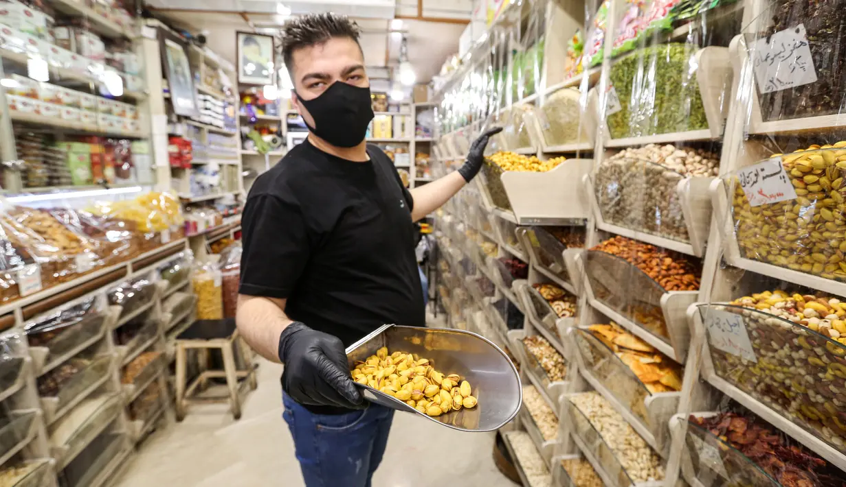 <p>Seorang pedagang buah kering mengenakan masker dan sarung tangan lateks, karena pandemi coronavirus COVID-19, memamerkan pistachio di tokonya di pasar Tajrish selama bulan suci Ramadan di Taheran, Iran (25/4/2020). (AFP/Atta Kenare)</p>