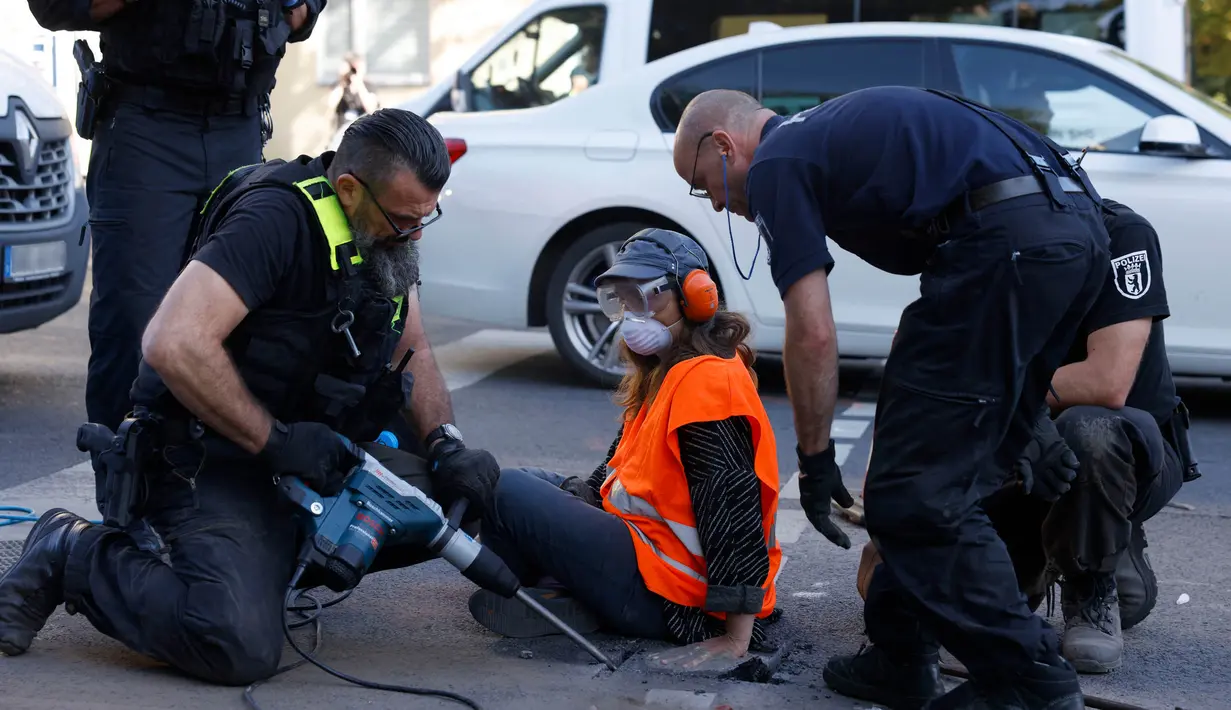 Polisi menggunakan alat untuk menyingkirkan sepotong permukaan jalan yang ditempeli oleh seorang aktivis iklim untuk menarik perhatian pada aksi keadaan darurat iklim, pada tanggal 18 September 2023 di Berlin. (Odd ANDERSEN/AFP)