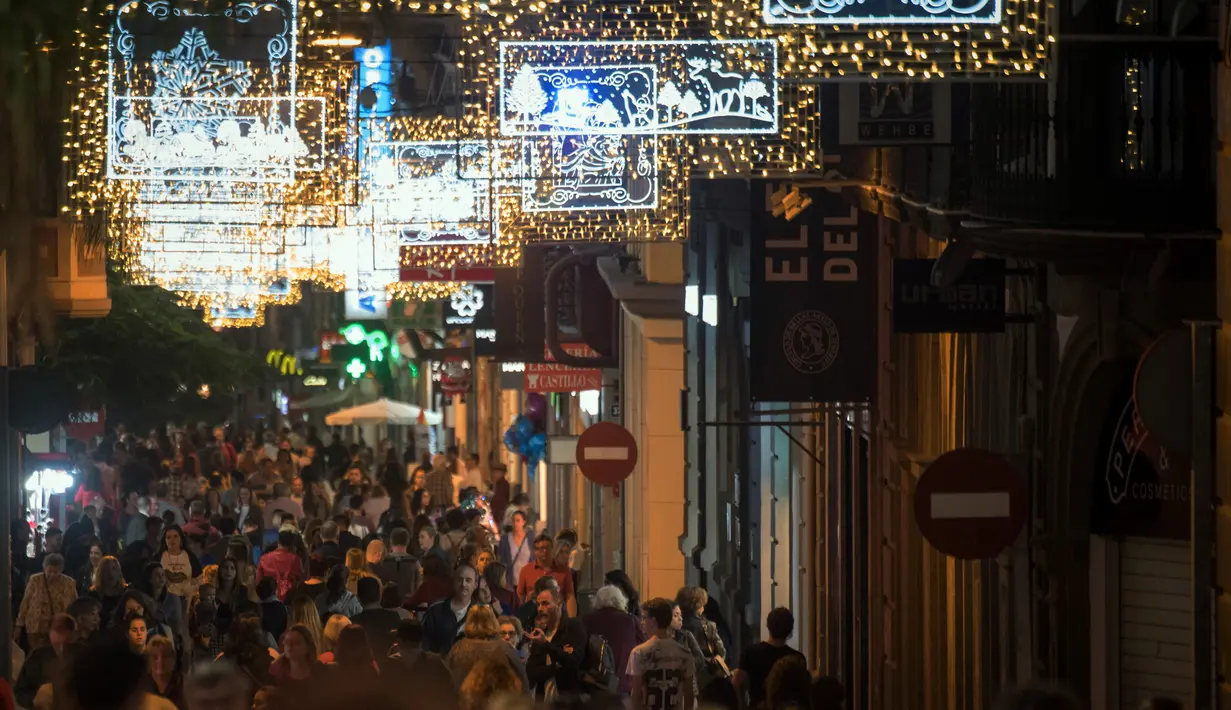 Orang-orang berjalan di bawah lampu Natal yang menghiasi jalan Santa Cruz de Tenerife di pulau Canary Tenerife, Spanyol (19/12). (AFP Photo/Desiree Martin)