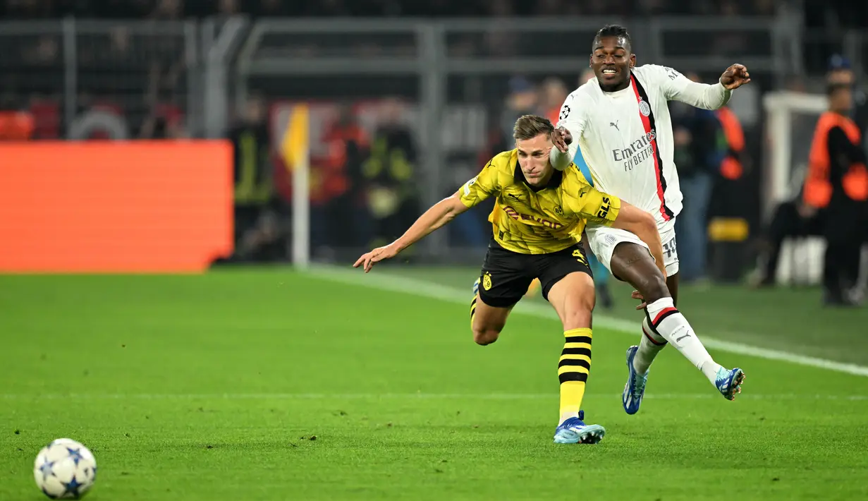 <p>Penyerang AC Milan, Rafael Leao (kiri) berebut bola dengan bek Borussia Dortmund, Nico Schlotterbeck, pada matchday 2 Grup F Liga Champions 2023/2024 di Signal Iduna Park, Kamis (5/10/2023) WIB. (INA FASSBENDER / AFP)</p>