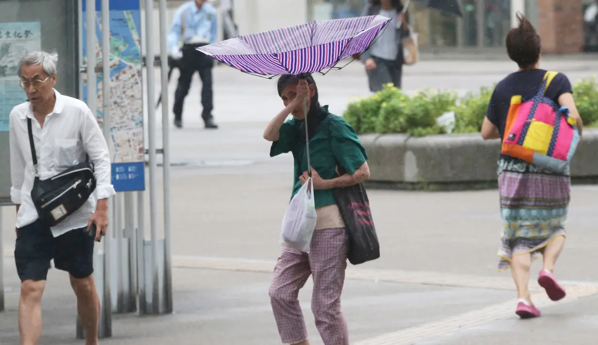 Seorang wanita berusaha memegangi payungnya saat angin kencang akibat topan jebi di Yokohama, dekat Tokyo, (4/9). PM Shinzo Abe mendesak warga segera dievakuasi dan meminta pemerintah mengambil seluruh langkah. (AP Photo/Koji Sasahara)
