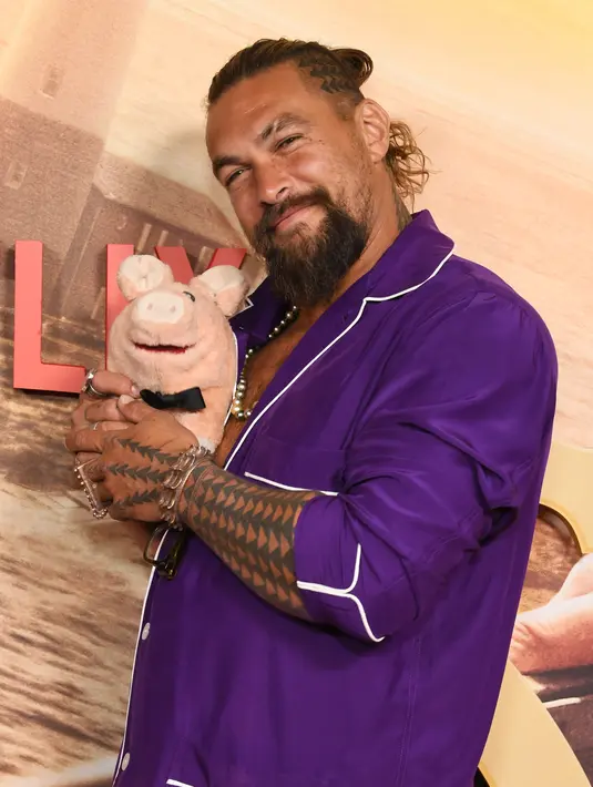 Jason Momoa berpose dengan boneka babi saat menghadiri pemutaran perdana film Netflix "Slumberland" di AMC Century City di Century City, California pada 9 November 2022. Ia membawa boneka babi setelah mengadopsi babi liarnya sendiri. (Jon Kopaloff/Getty Images/AFP)