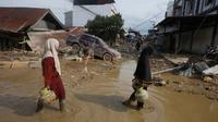 Hingga Kamis (5/12/2025) malam, listrik belum menyala, sehingga jalanan masih gelap gulita. Tampak dalam foto, para penyintas berjalan melewati reruntuhan mobil di area terdampak banjir bandang di Aceh Tamiang, Sumatera, Indonesia, Kamis 4 Desember 2025. (AP Photo/Binsar Bakkara)