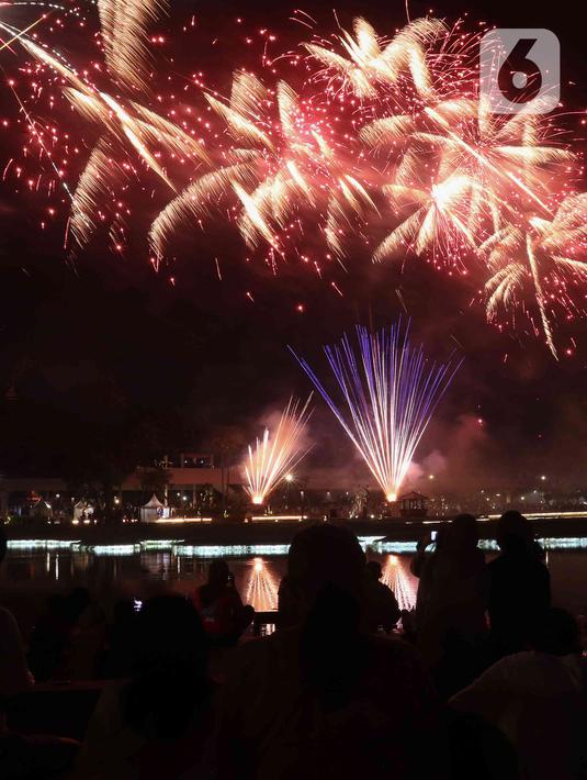 Warga menyaksikan pesta kembang api saat perayaan malam puncak Tahun Baru 2023 di Danau Archipelago, Taman Mini Indonesia Indah (TMII), Jakarta, Minggu (1/1/2023). Kembang api yang diluncurkan sangatlah indah dan beragam. Baik dari perpaduan warna, letupan, hingga perpaduan terbangnya yang beragam. (Liputan6.com/Herman Zakharia)