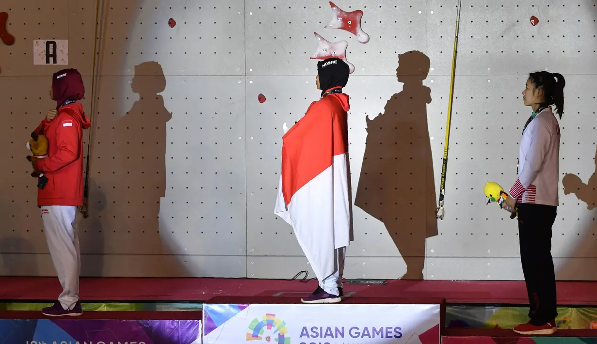 Peraih medali emas Indonesia Susanti Rahayu Aries (tengah), medali perak Puji Lestari dan perunggu He Cuilian mendengarkan lagu Indonesia Raya pada upacara medali olahraga panjat tebing wanita Asian Games 2018 di Palembang (23/8). (AFP PHOTO / Adek Berry)