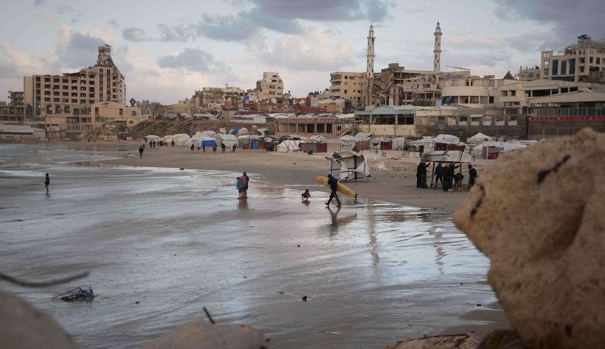 Warga Palestina menata kembali kehidupan mereka di antara puing-puing kehancuran akibat serangan yang dilancarkan Israel sejak Okrober 2023 silam. Tampak dalam foto, seorang peselancar Palestina membawa papan selancarnya ke laut di sepanjang garis pantai di Kota Gaza, Minggu, 28 Desember 2025. (AP Photo/Jehad Alshrafi)