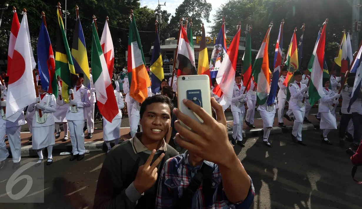 Warga berselfie saat melihat arak-arakan bendera di kawasan Bundaran HI, Jakarta, Minggu (30/10). Parade ini merupakan rangkaian arak-arakan parade Bendera Menjelang Sidang Umum Interpol Ke-85. (Liputan6.com/Johan Tallo)