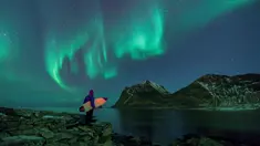 Seorang peselancar menatap Aurora sebelum beraksi di Lofoten Islands, Norwegia, (9/3/2018). Suhu udara minus 13°C dan suhu diatas air sekitar 4°C. (AFP/Oliver Morin)