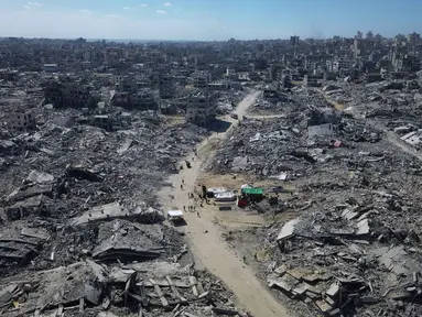 Foto udara yang diambil menggunakan pesawat tanpa awak atau drone memperlihatkan beberapa warga Palestina berjalan di sepanjang jalan yang dikelilingi oleh bangunan-bangunan yang hancur akibat serangan militer Israel selama dua tahun terakhir di Kota Gaza, Rabu 15 Oktober 2025. (AP Photo)