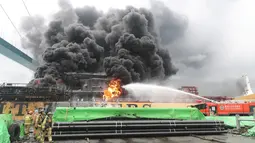 Petugas pemadam kebakaran menyeprotkan air ke arah kapal kargo yang terbakar di pelabuhan Ulsan, di pantai tenggara Korea Selatan (28/9/2019). Menurut pihak berwenang, sembilan pelaut terluka setelah kebakaran terjadi di kapal kargo dan menyebar ke kapal lainnya. (AFP/Yonhap)