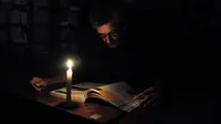 Seorang pria membaca dengan menggunakan lilin akibat pemadaman listrik di San Cristobal, Venezuela, Senin (25/4). Venezuela menerapkan pemadaman listrik selama empat jam sehari untuk menghadapi krisis energi yang memburuk. (GEORGE Castellanos/AFP)
