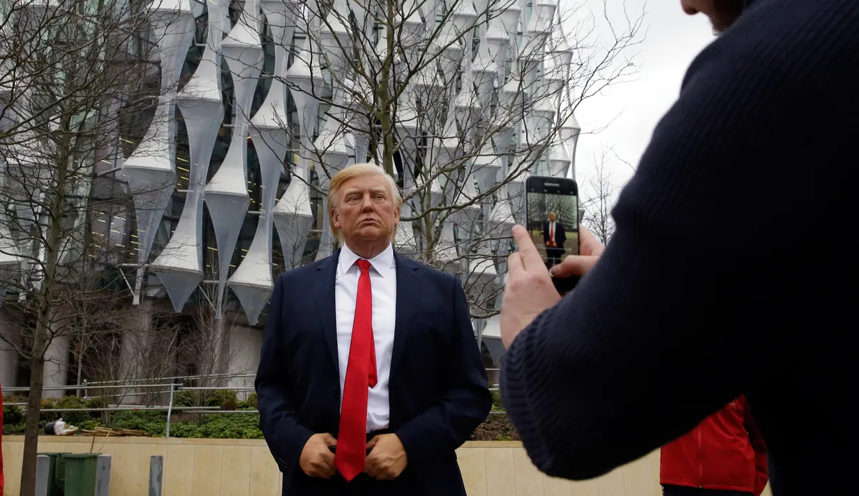 Seorang pria mengambil gambar lilin Madame Tussauds Presiden AS Donald Trump yang dipajang di luar Kedutaan Besar AS yang baru di Nine Elms, London (12/1). Donald Trump telah membatalkan rencana kunjungannya ke London. (AP Photo / Alastair Grant)