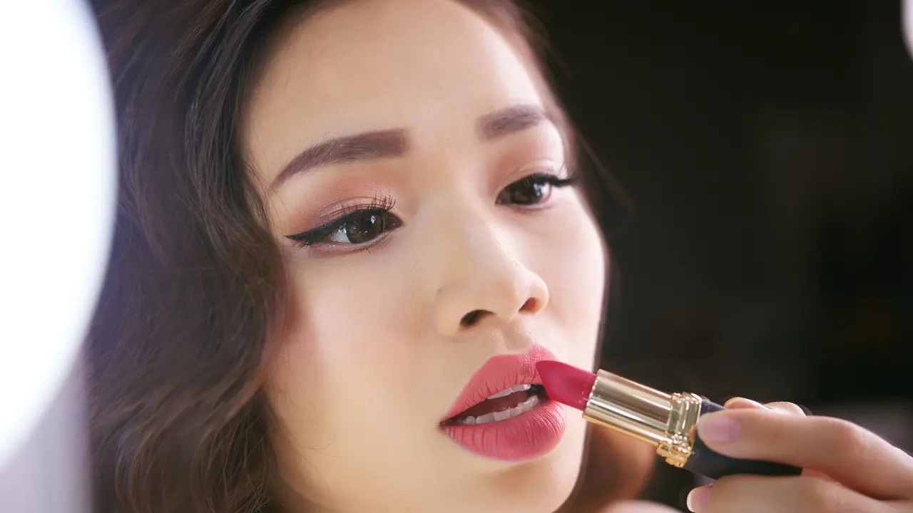 Seorang perempuan sedang mengaplikasikan lipstik di bibirnya (Foto Dok: Freepik/pressfoto)