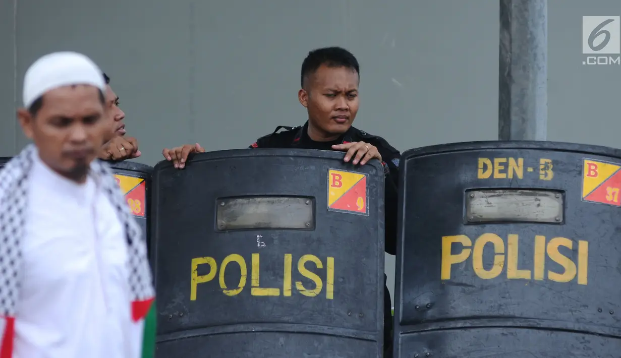 Petugas berjaga di belakang tameng saat aksi dukungan bagi negara Palestina di depan Kedubes AS, Jakarta, Minggu (10/12). Mereka memprotes keputusan Presiden Trump yang mengakui Yerusalem jadi Ibu Kota Israel. (Liputan6.com/Helmi Fithriansyah)