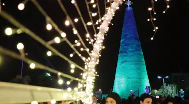 Orang-orang berkumpul di sekitar Pohon Natal raksasa yang terbuat dari botol plastik di kota Chekka, Lebanon, 15 Desember 2019. Sebanyak 129 ribu botol plastik ditata untuk menjadi pohon Natal setinggi 28.5 meter.  (Ibrahim CHALHOUB/AFP)