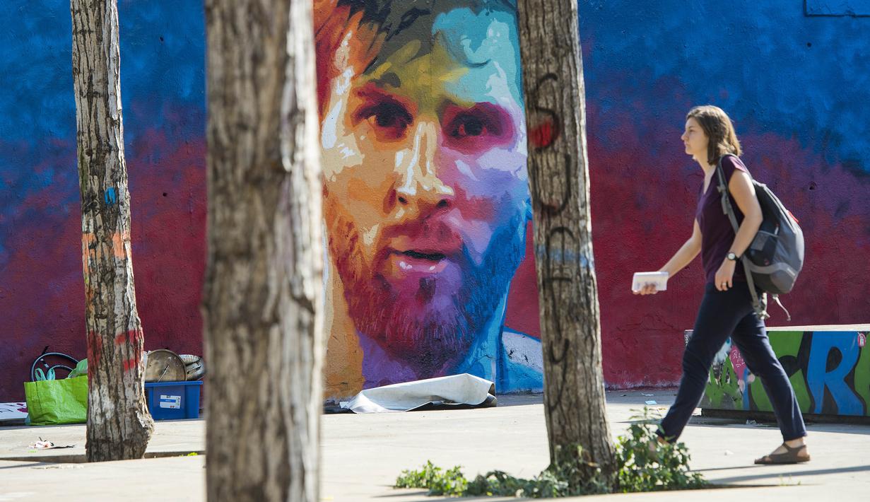 Seorang wanita melintasi mural bergambar wajah bintang Barcelona, Lionel Messi, yang terdapat di Barcelona, Catalonia, Sabtu (17/6/2017). (AFP/Josep Lago)
