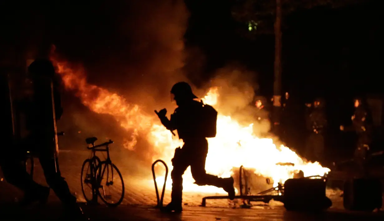 Petugas kepolisian melewati api yang dinyalakan oleh demonstran saat berunjuk rasa di Hamburg, Kamis (6/7). Polisi antihuru-hara Jerman bentrok dengan para pengunjuk rasa menjelang pertemuan puncak KTT G20 yang digelar pada 7-8 Juli. (AP/Markus Schreiber)
