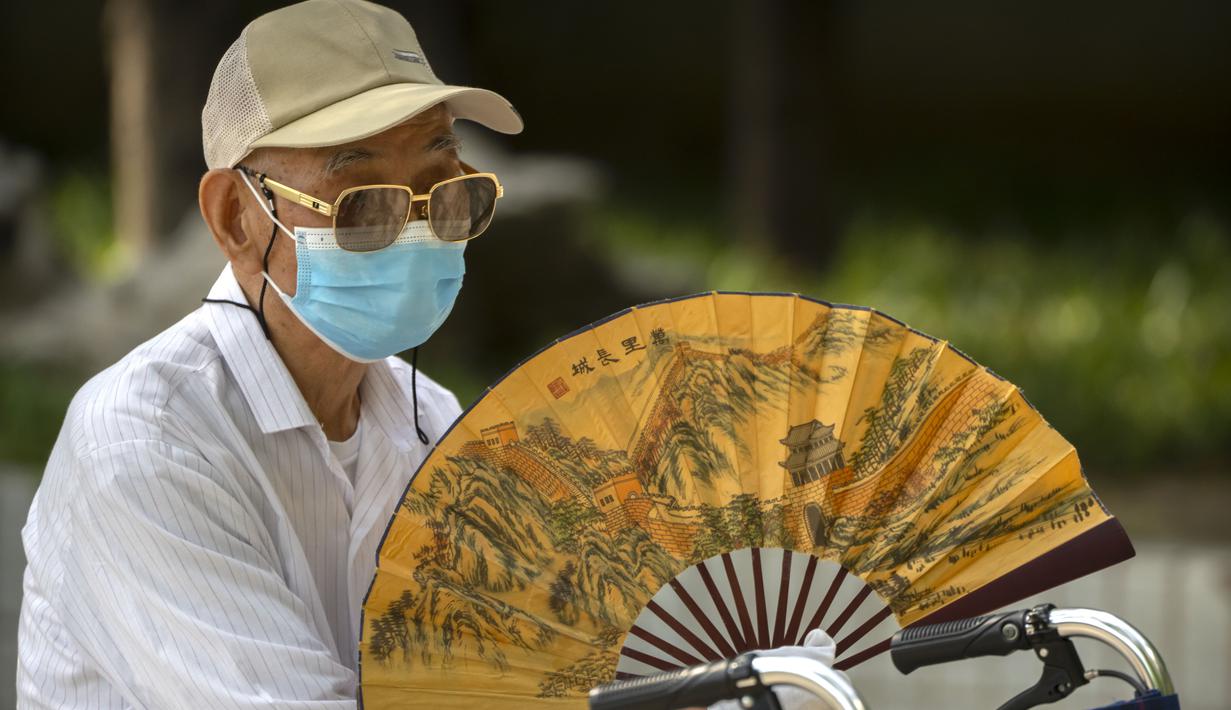 Seorang pria tua yang mengenakan masker mengipasi dirinya sendiri di sebuah taman umum di Beijing, Jumat (8/7/2022). Ibu kota China, Beijing, tampaknya telah membatalkan rencana untuk mengeluarkan mandat yang mengharuskan orang menunjukkan bukti vaksinasi COVID-19 untuk masuk ke ruang publik tertentu setelah penolakan di kalangan penduduk. (AP Photo/Mark Schiefelbein)
