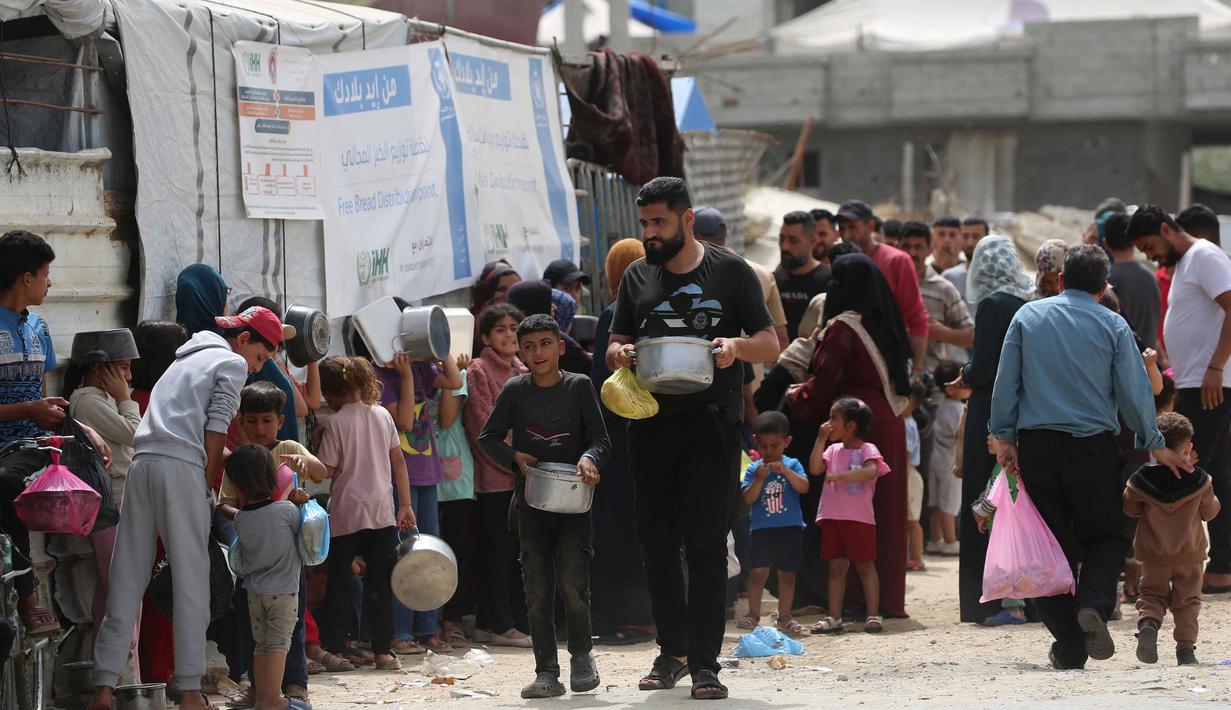 Keluarga-keluarga Palestina yang mengungsi sambil memegang wadah kosong menunggu giliran untuk mengambil makanan dari dapur amal, di kamp pengungsi Bureij, Jalur Gaza Tengah pada Senin 18 Mei 2026. (Eyad Baba/AFP)