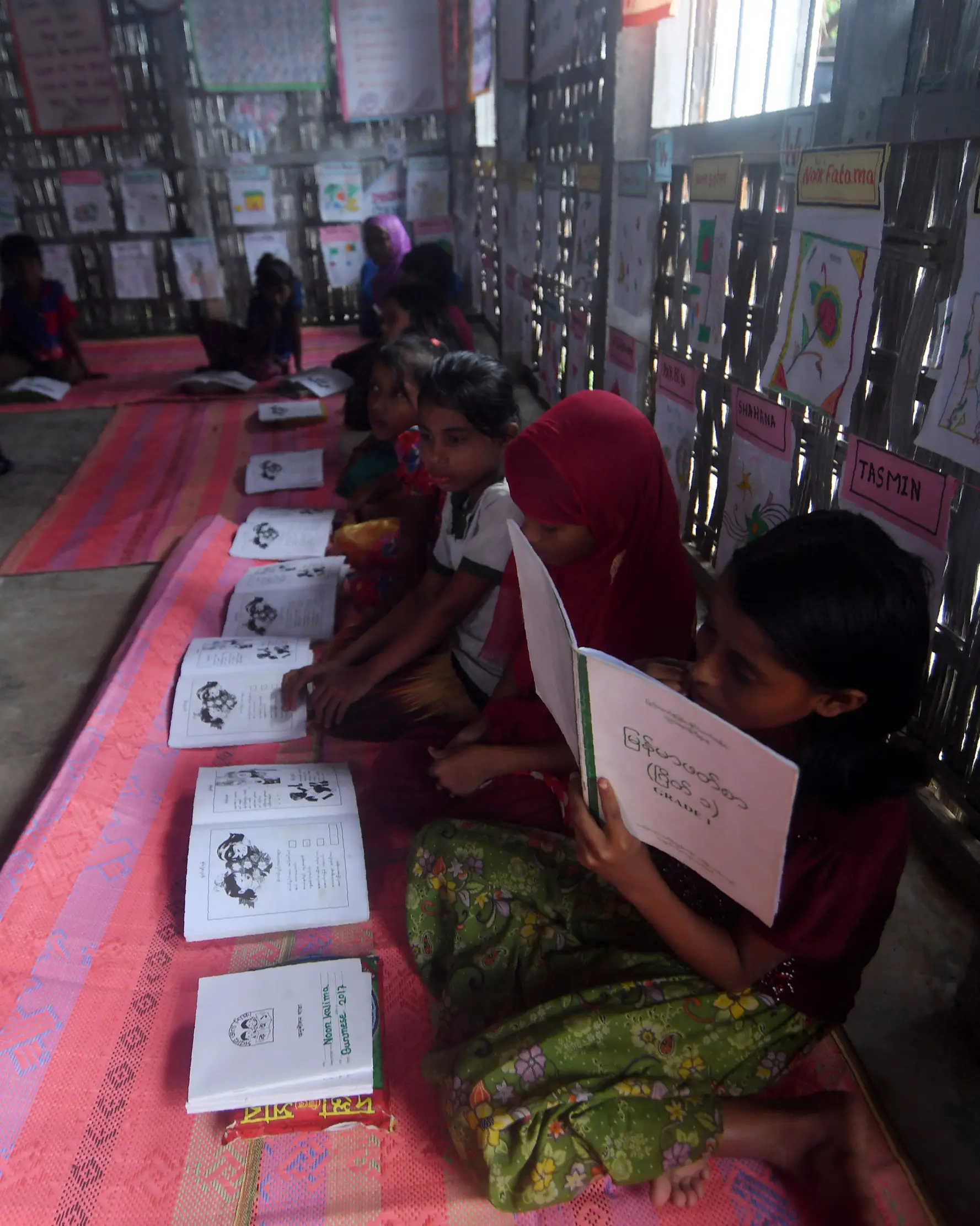 Anak-anak pengungsi Rohingya belajar dengan beralaskan tikar di sebuah sekolah darurat di kamp pengungsian di Teknaf, Bangladesh, 8 Oktober 2017. Dengan fasilitas seadanya, para relawan memberikan pendidikan kepada bocah-bocah itu. (MUNIR UZ ZAMAN / AFP)