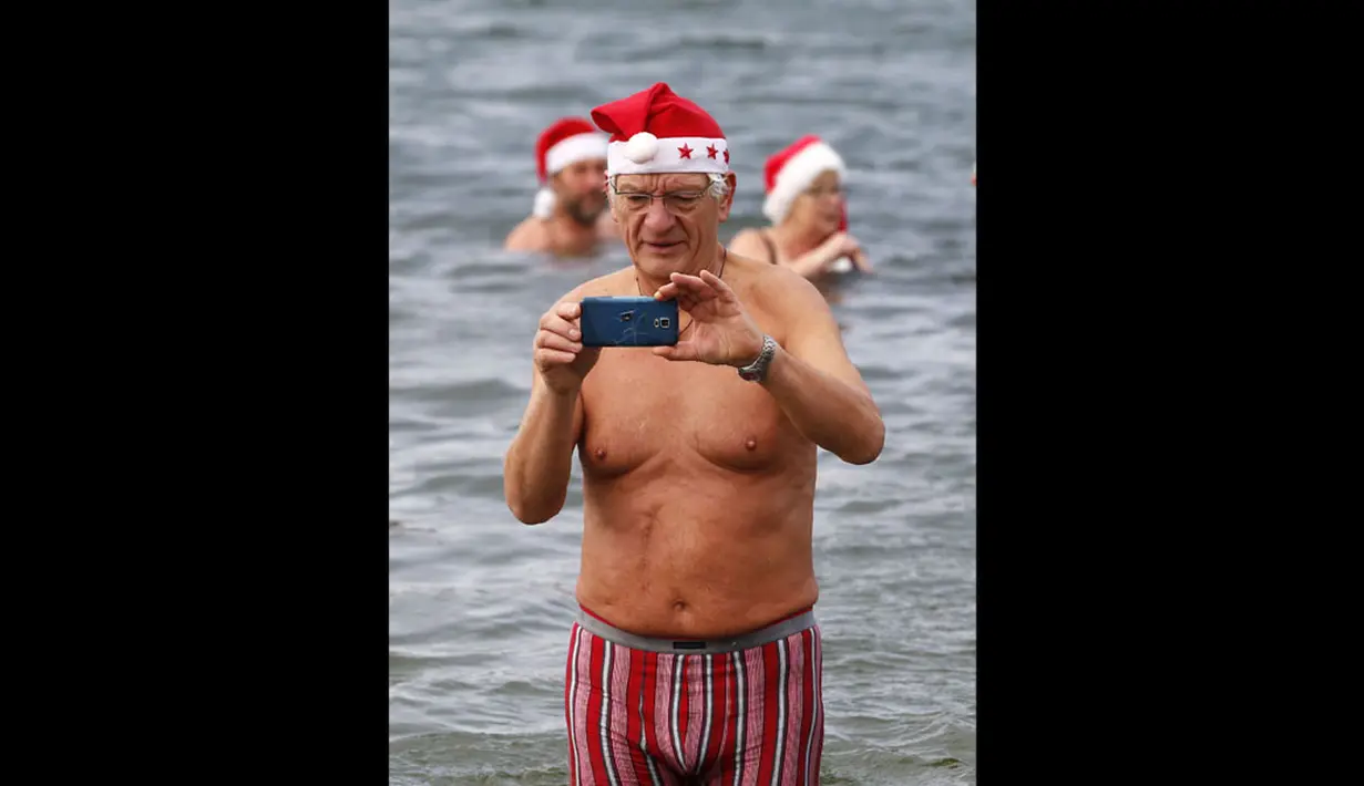 Puluhan anggota klub renang es "Berliner Seehunde" merayakan Natal dengan berenang di danau Orankesee, Berlin (25/12/2014). Tampak, seorang anggota klub "Berliner Seehunde" mengambil gambar dengan telepon genggamnya. (REUTERS/Fabrizio Bensch)