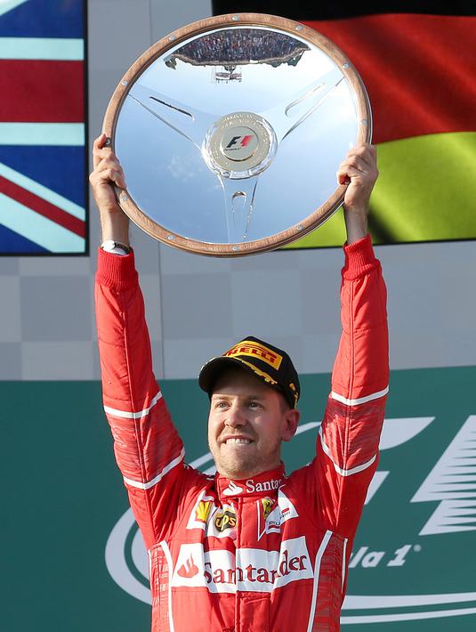 Pembalap Ferrari, Sebastian Vettel berpose dengan trofinya setelah memenangi balapan GP Australia di Sirkuit Albert Park, Melbourne, Minggu (26/3). Sebastian Vettel finis dengan catatan waktu tercepat 1 jam 24 menit 11,672 detik. (AP Photo/Rick Rycroft)