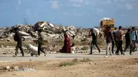 Otoritas Gaza menyeru kepada dunia internasional untuk menekan Israel agar menghentikan agresi serta membuka jalur bantuan tanpa hambatan. Tampak dalam foto, warga Palestina, membawa tas dan kardus kosong, berjalan melewati bangunan yang hancur saat mereka kembali dari titik distribusi makanan yang dikelola oleh Yayasan Kemanusiaan Gaza (GHF) yang didukung AS dan Israel, di dekat koridor Netsarim di Jalur Gaza tengah pada 5 Oktober 2025. (Eyad BABA/AFP)