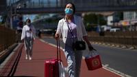 Seorang wanita mengenakan masker berjalan dengan barang bawaannya di jalan saat dia meninggalkan stasiun kereta api Beijing di Beijing, Selasa (6/9/2022). China lockdown jutaan warganya di bawah pembatasan ketat COVID-19 dan melarang warganya lakukan perjalanan domestik pada hari libur nasional yang akan datang. (AP Photo/Andy Wong)