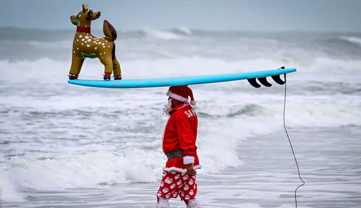 Seorang pengunjung berkostum Sinterklas bersiap untuk berselancar dalam acara Surfing Santa yang berlangsung di Pantai Cocoa, Florida, Amerika Serikat, Selasa (24/12/2024) waktu setempat. (AFP/Giorgio Viera)